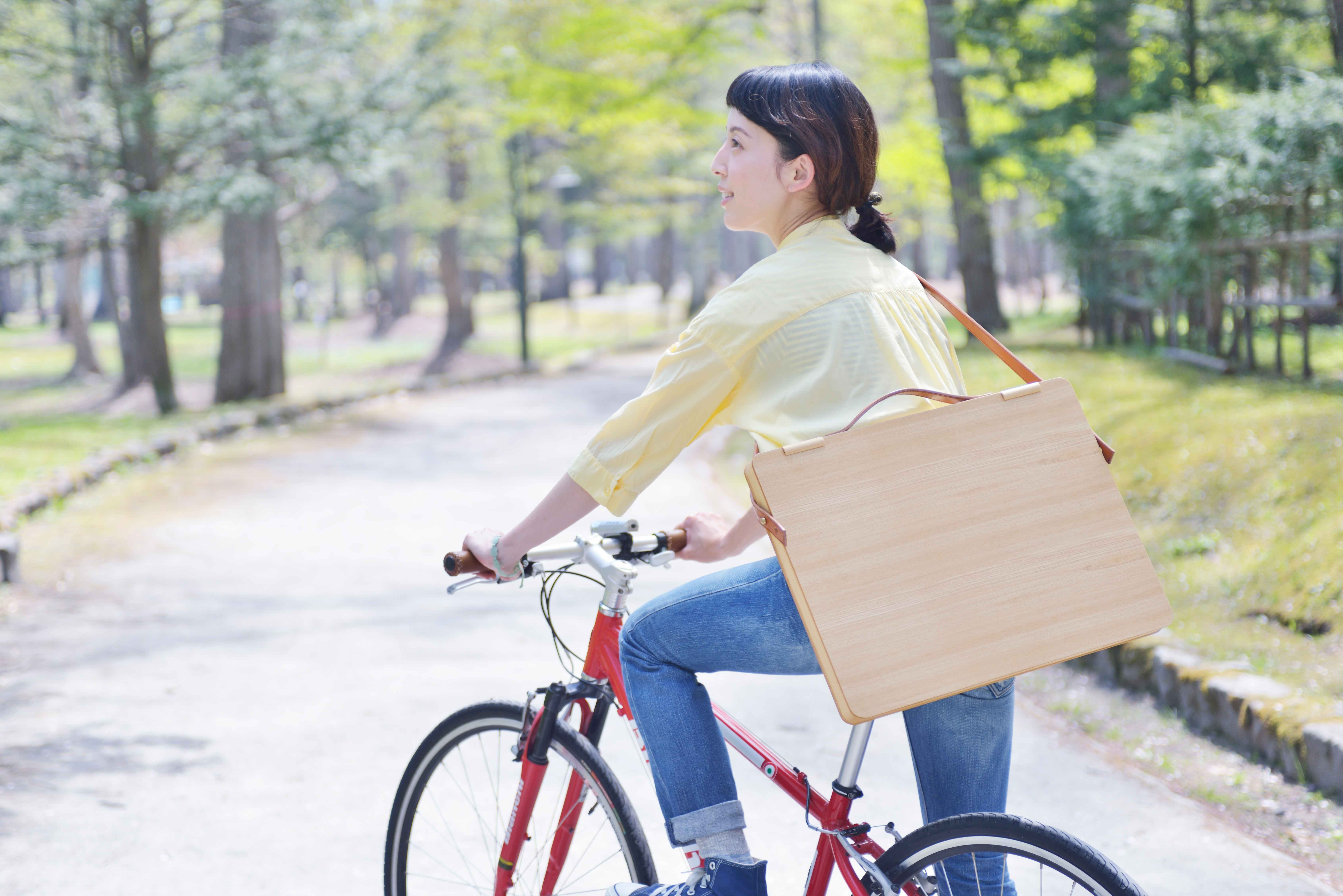 女性が自転車に乗り木製ポートフォリオケースを持っている